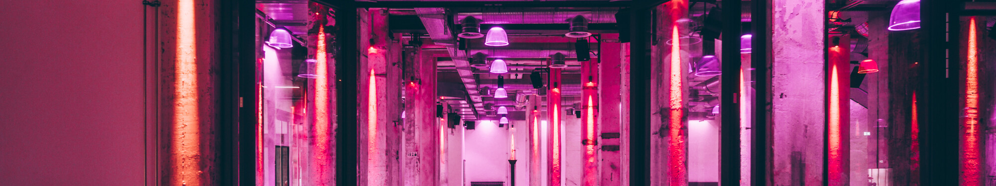 Die Stützpfeiler im Foyer der Grand Hall Zollverein in Essen sind mit rotem und violettem Neonlicht beleuchtet.  