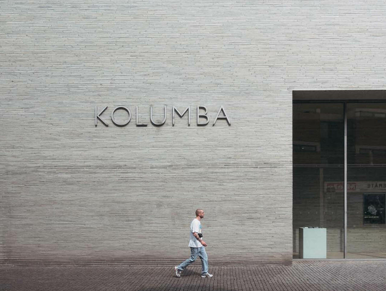 Ein Mensch läuft an der grauen Fassade mit Schriftzug Kolumba am Museum Kolumba in Köln vorbei.  