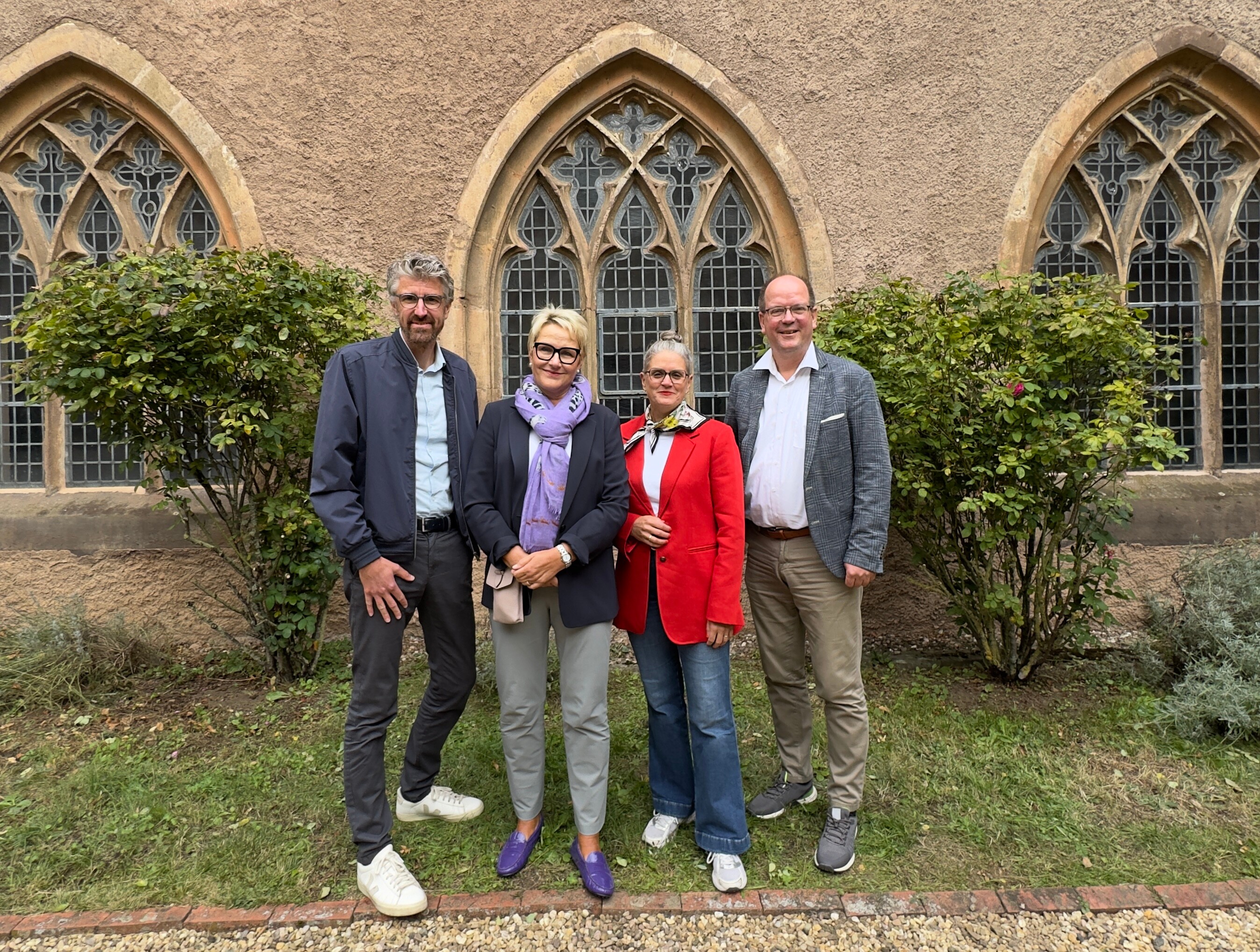 Die beiden Vorstandsmitglieder von Tourismus NRW stehen mit den beiden Vorsitzenden des Ausschusses für Destinationsmarketing des Verbands vor großen Kirchenfenstern. 