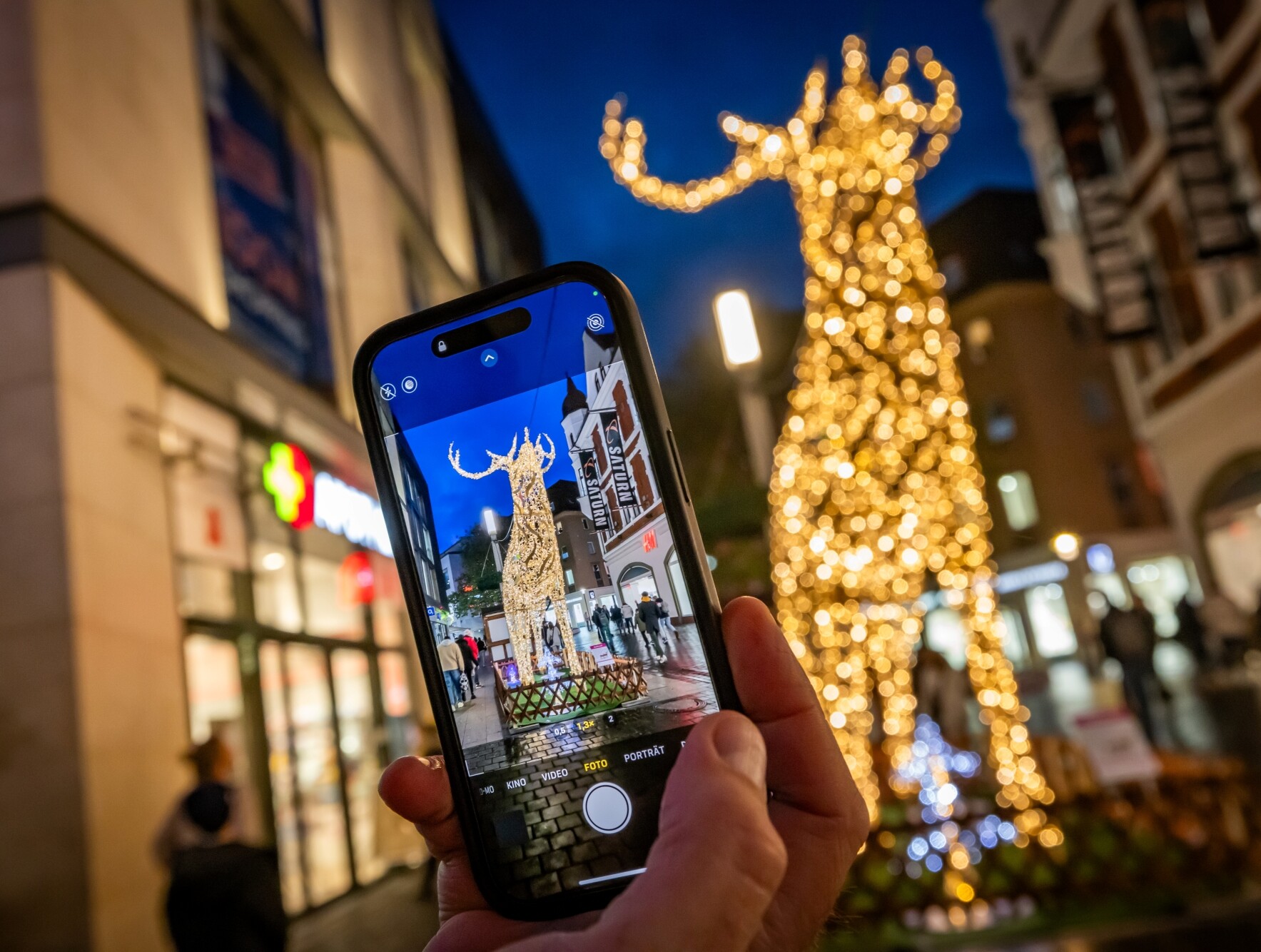 Ein Mensch hält ein Handy vor eine leuchtende Hirsch-Skulptur in der Bielefelder Innenstadt.  