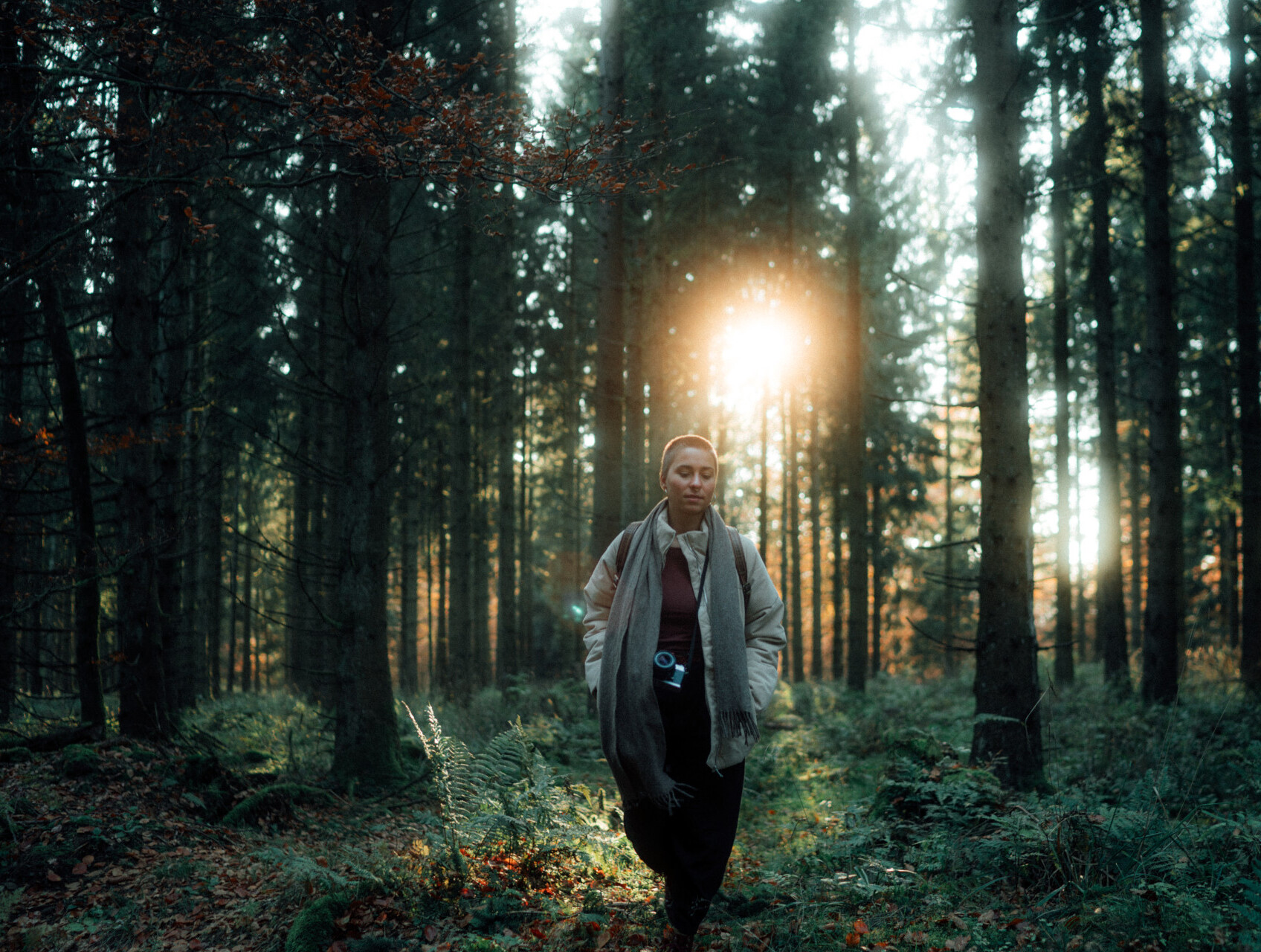 Eine Frau läuft durch einen Fichtenwald im Rothaargebirge. Durch die Bäume scheint die Sonne. 