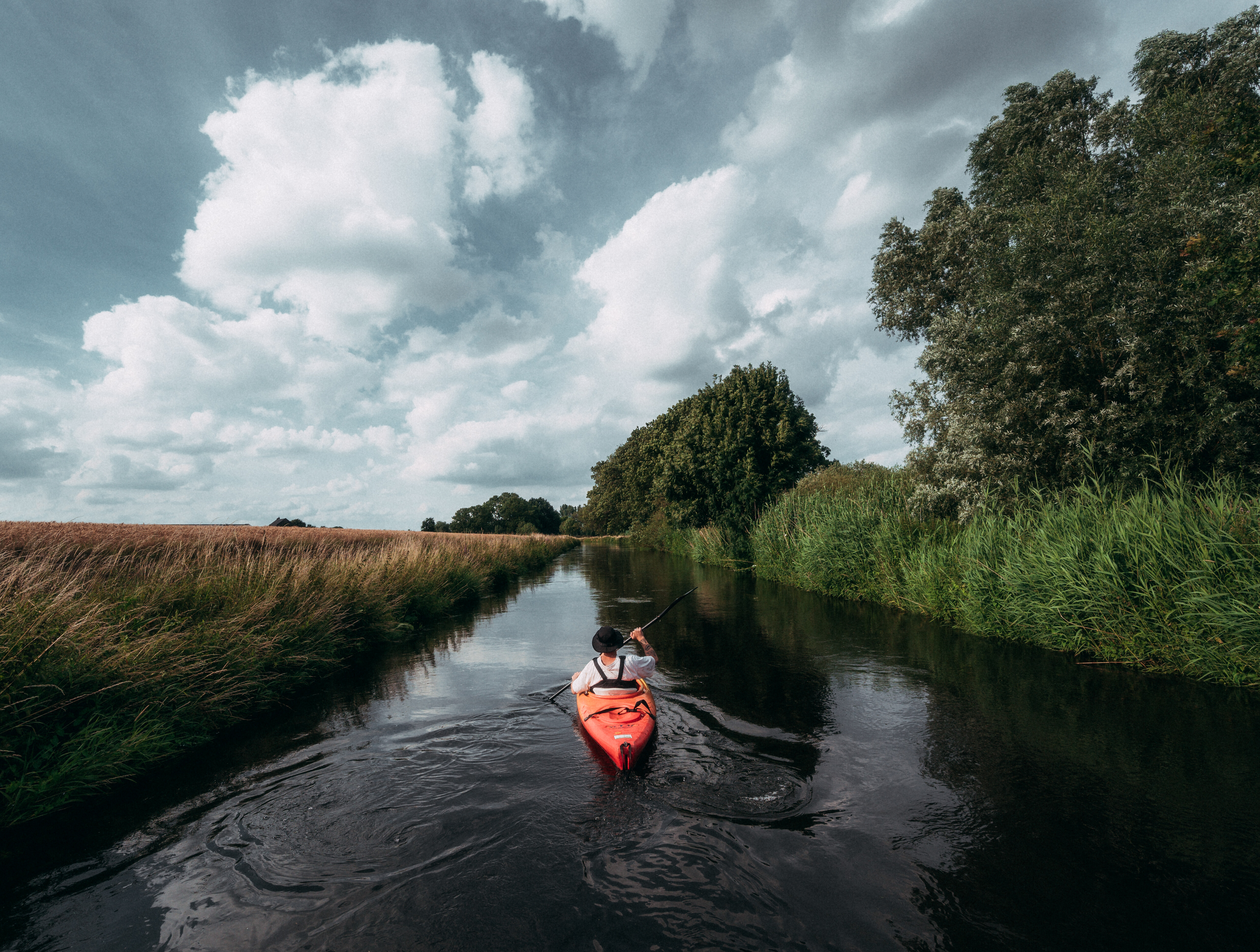Ein Mensch fährt mit einem roten Kajak fahren auf der Niers am Niederrhein. Die Flussauen sind dicht mit Gräsern und Bäumen bewachsen.  © Tourismus NRW e.V./Johannes Höhn