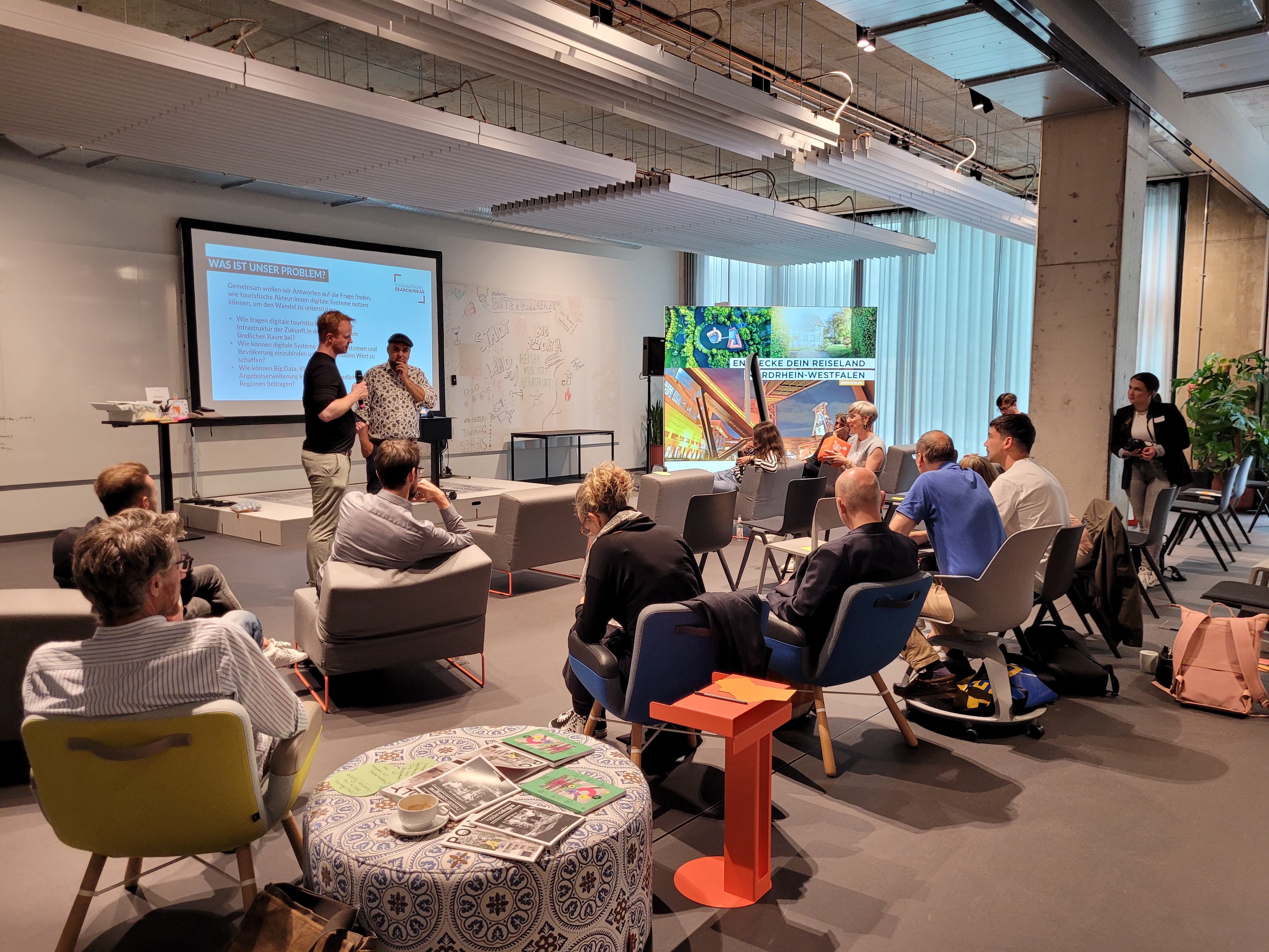 Menschen sitzen beim Hackathon Search:Ideas auf Stühlen und hören einem Redner zu 