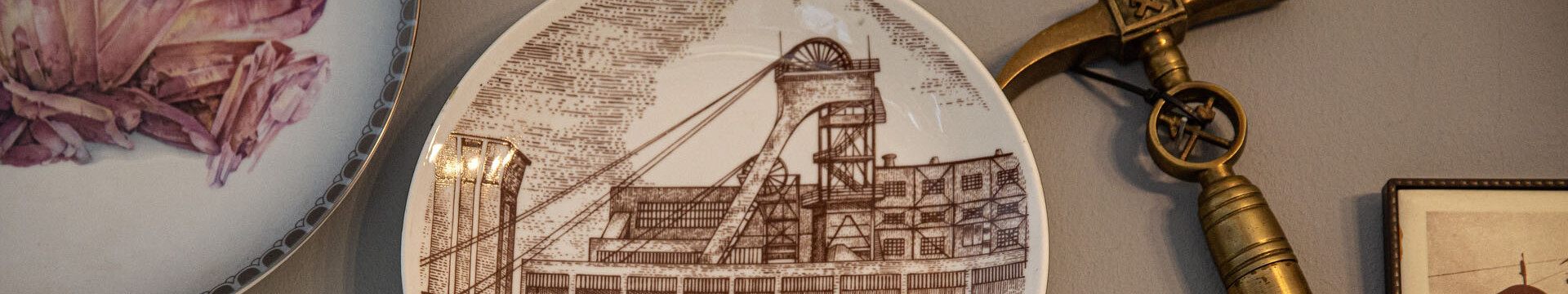Ein Motivteller mit der Abbildung des Bergwerks Westerholt und ein Hammer hängen als Andenken an den Bergbau im Ruhrgebiet an einer Wand. 