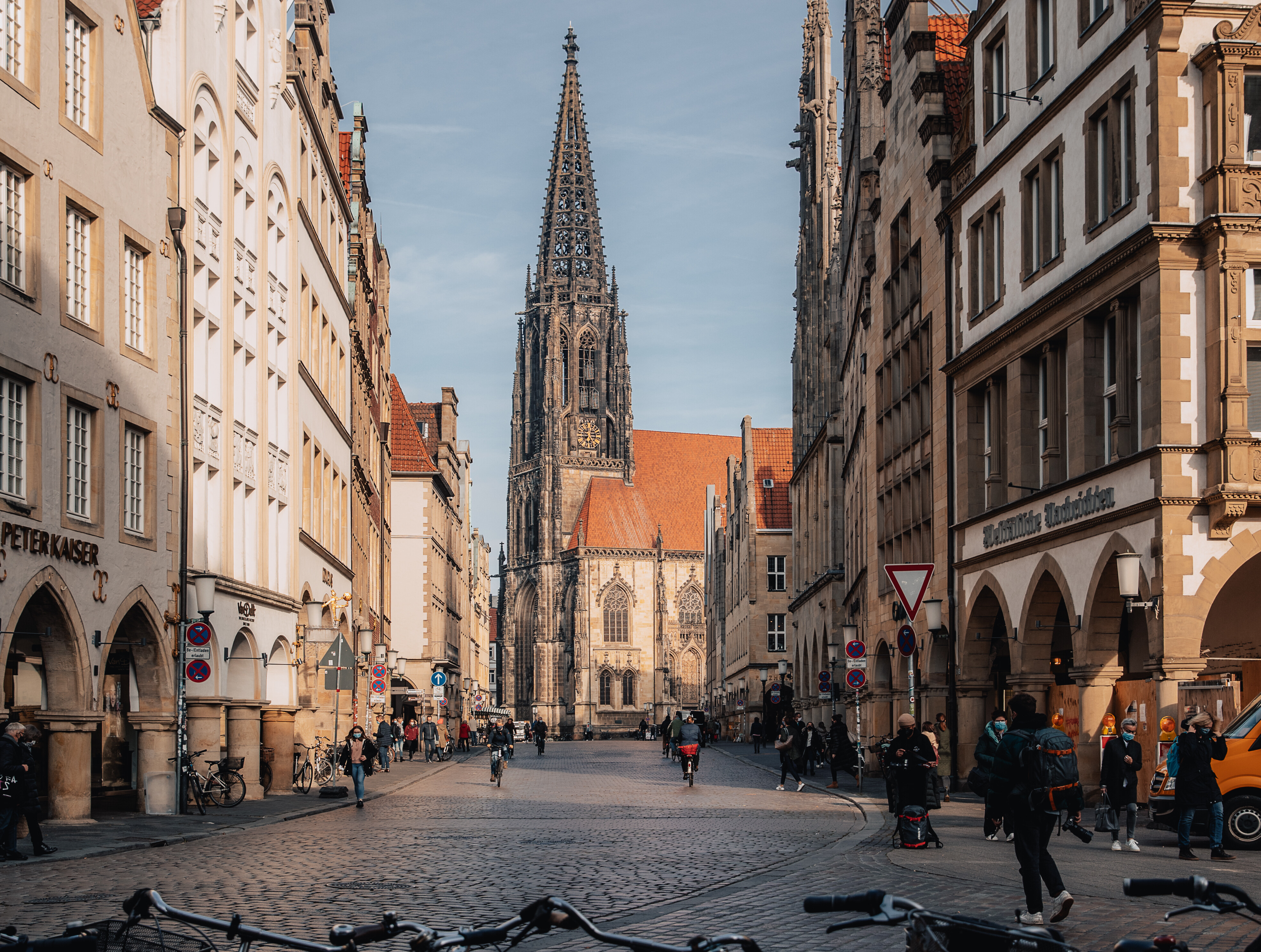 Blick auf den Prinzipalmarkt und die Lamberti-Kirche in Münster. Durch die Straße fahren viele Menschen auf Fahrrädern.  