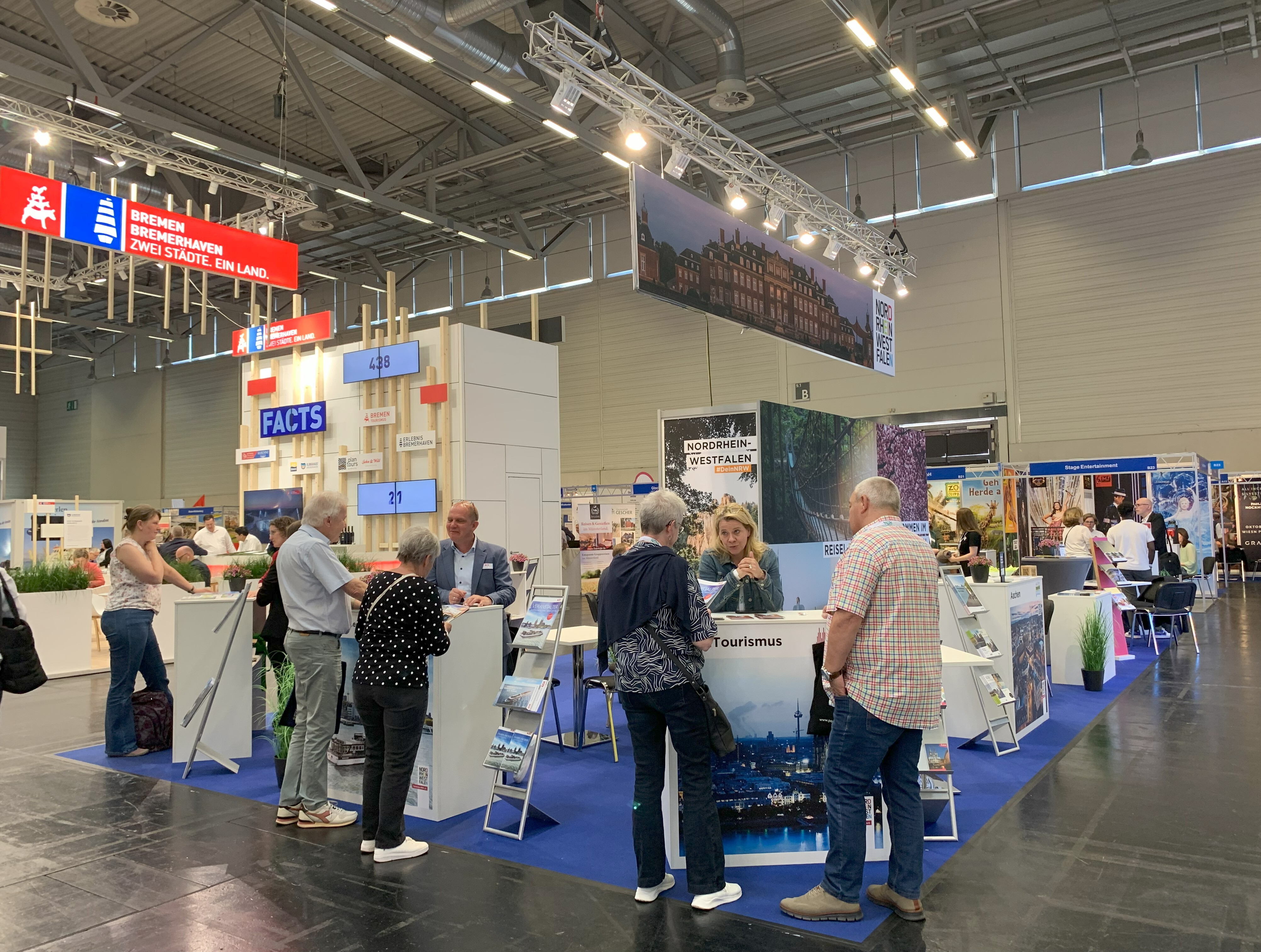 RDA Group Travel Expo 2025 © Tourismus NRW e.V. NRW-Messestand auf der RDA Group Travel Expo in Köln mit mehreren Personen im Gespräch. Über dem NRW-Stand hängt ein großes Foto von Schloss Nordkirchen im Münsterland.