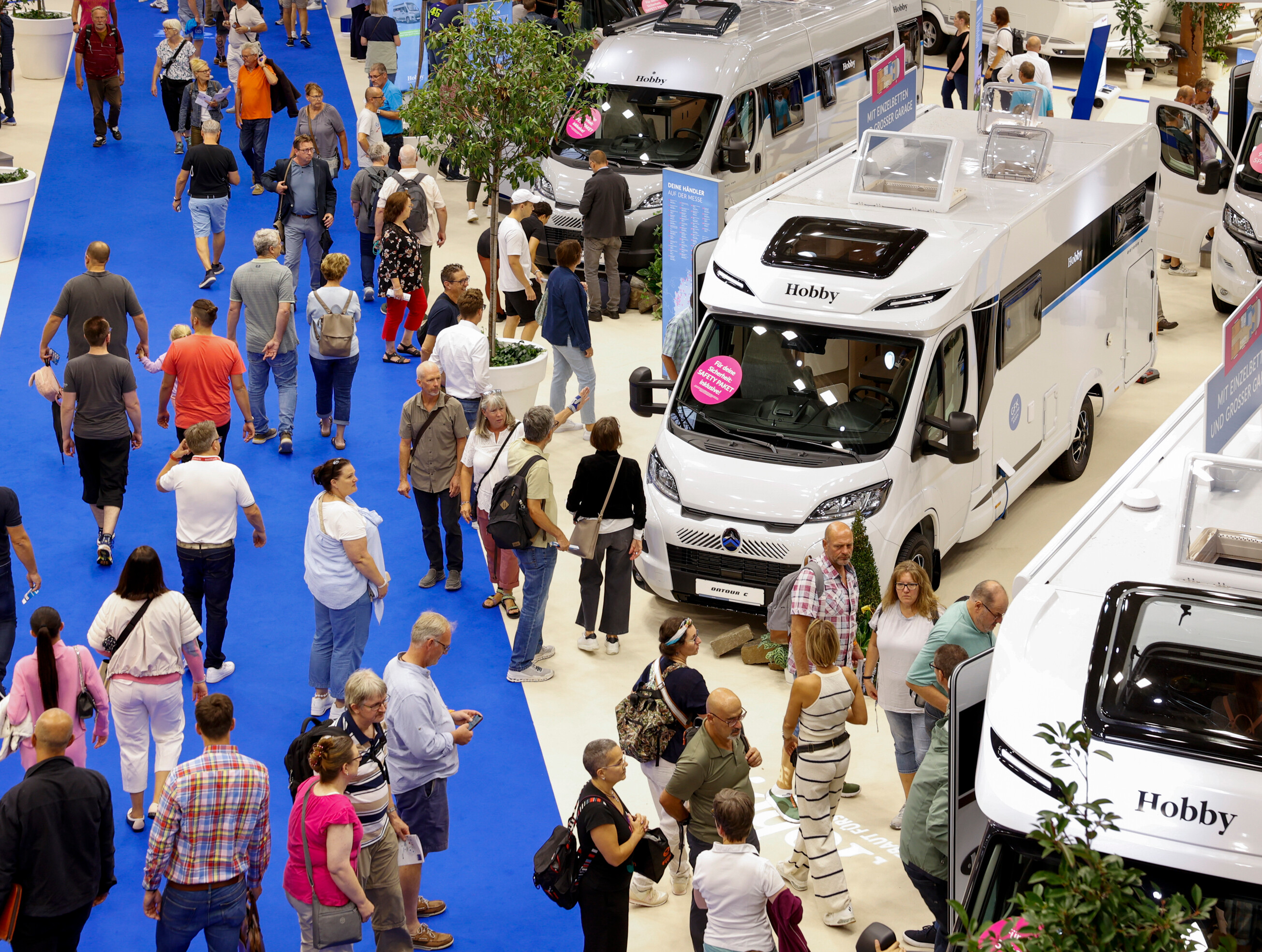 Caravan Salon 2024 © Messe Düsseldorf/ct Menschenmenge auf einem blauen Teppich in einer Messehalle der Messe Düsseldorf beim Caravan Salon 2024. umgeben von Wohnmobilen. Besucher betrachten die Fahrzeuge und stehen teilweise in Schlangen, um sie von innen zu besichtigen.