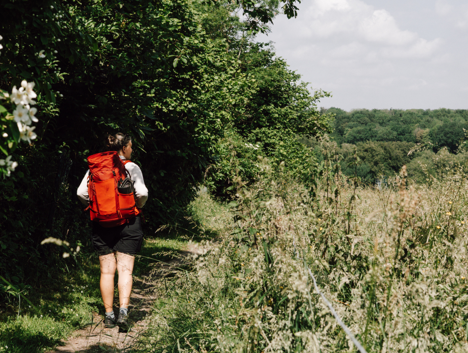 Niederländische Bloggerin mit großem roten Rucksack wandert über einen schmalen Pfad unter Bäumen.