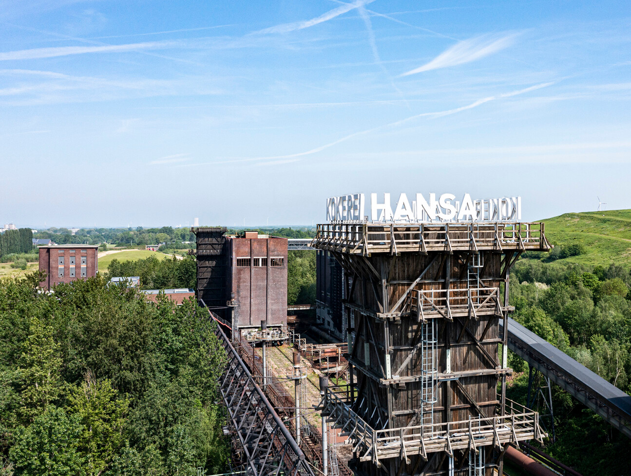 Turm der Kokerei Hansa in Dortmund, umgeben von Bäumen und dem grünen Deusenberg, einem rekultivierten Deponiegelände