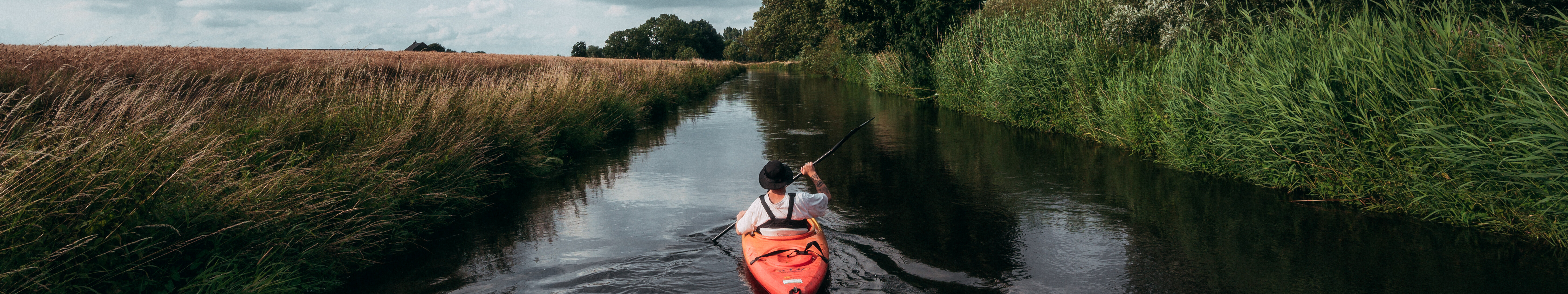 Kajakfahren auf der Niers © Tourismus NRW e.V./Johannes Höhn Ein Mensch fährt mit einem roten Kajak fahren auf der Niers. Die Flussauen sind dicht mit Gräsern und Bäumen bewachsen.