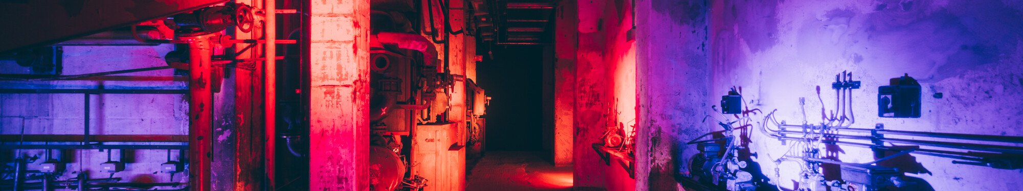 Blick in die ehemalige, mit rotem und violettem Neonlicht beleuchtete Fabrikanlage des heutigen Unesco-Welterbes Zollverein in Essen. © Tourismus NRW e.V./Johannes Höhn