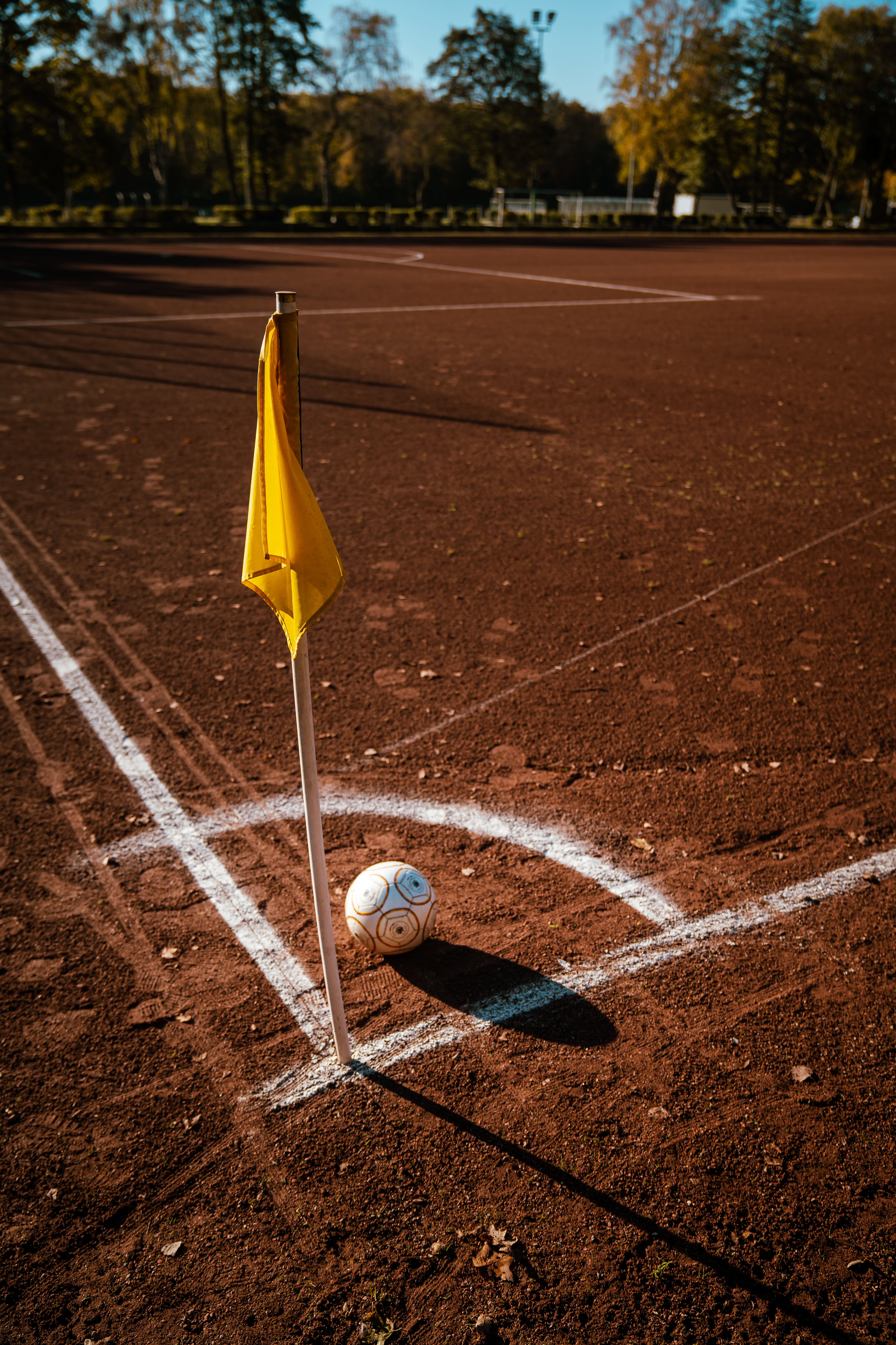 Das Bild zeigt eine Eckfahne auf einem Fußball-Ascheplatz. Im weiß umrandeten Eckfeld liegt ein weißer Fußball zum Abschuss bereit.