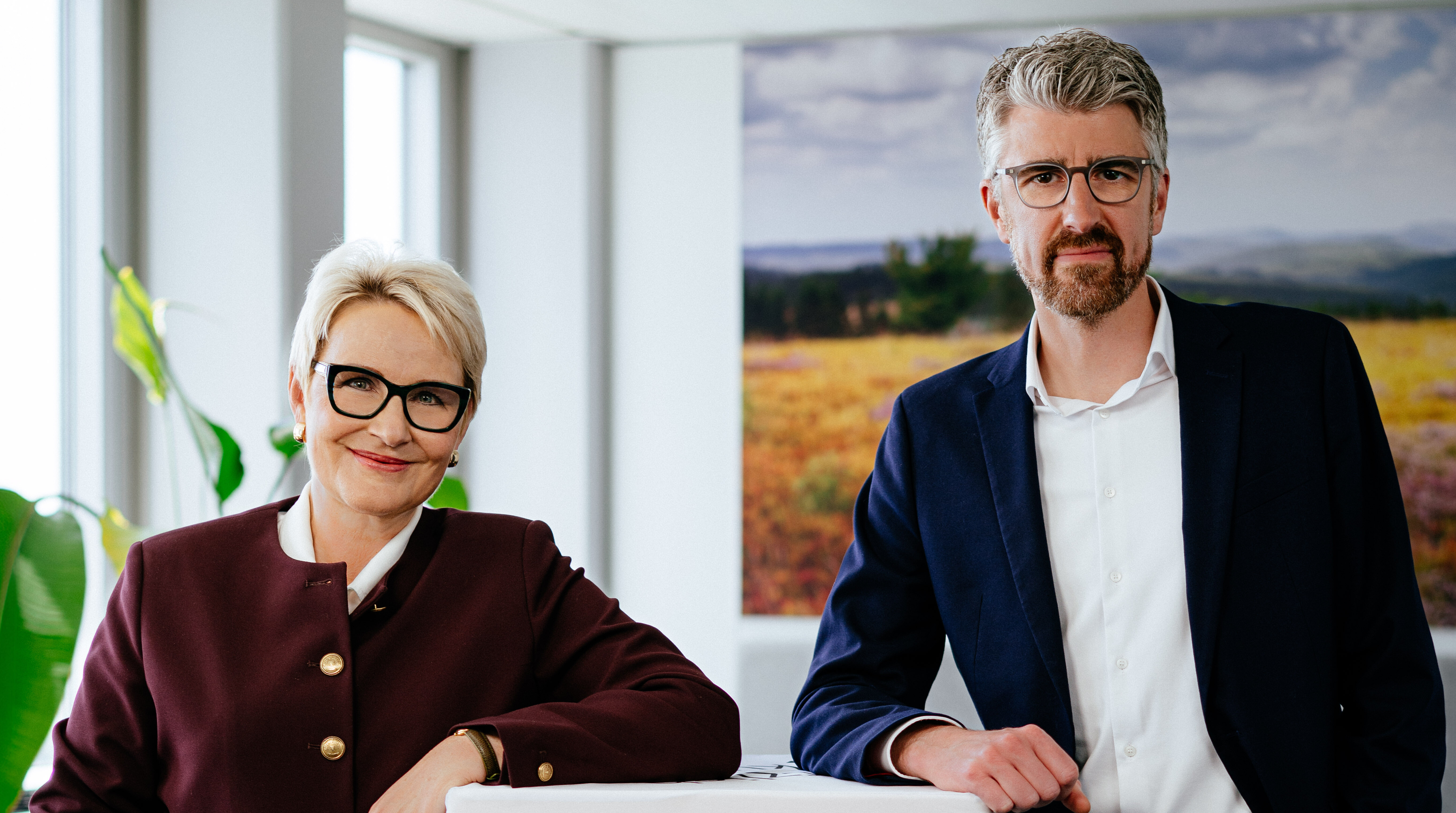 Die Vorstandsvorsitzende von Tourismus NRW, Dr. Heike Döll-König, und ihr Stellvertreter, Sebastian Kaiser, stehen in einem Konferenzraum neben einem großen Würfel, auf dem das Logo des Reiselands Nordrhein-Westfalen zu sehen ist. 