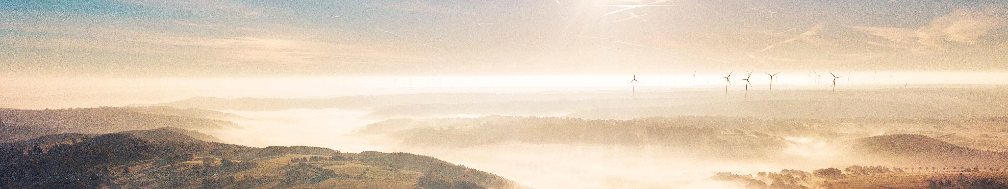 Bei Sonnenaufgang liegt Nebel über den Wiesen und Wäldern der Eifel. 