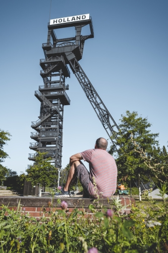 Ein Mann sitzt auf einer Mauer vor dem Förderturm der Zeche Holland in Bochum