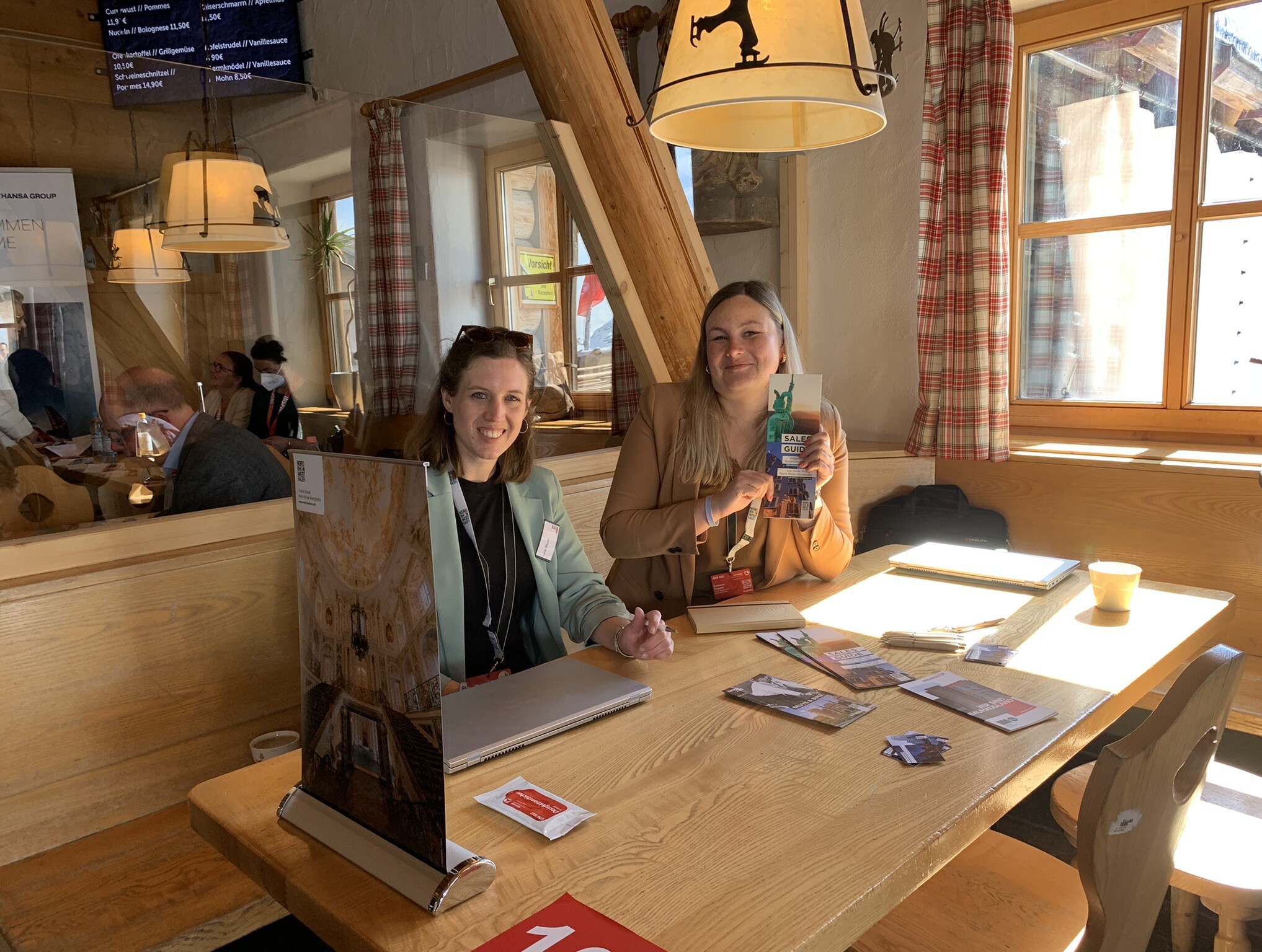 Zwei Mitarbeiterinnen des Tourismus NRW sitzen an einem Tisch mit Werbeprospekten zum Reiseland Nordrhein-Westfalen.