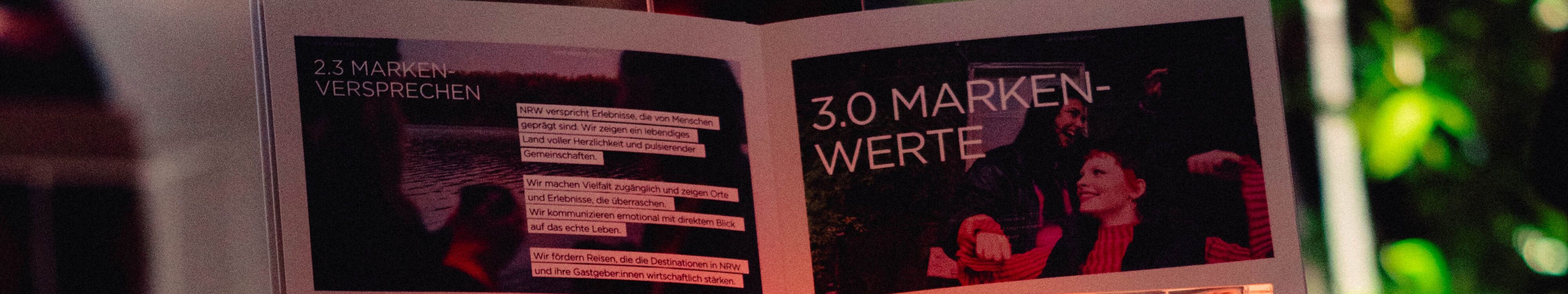 Neuer Markenauftritt von DeinNRW © Thomas Kaup/RP Creatives, Tourismus NRW e.V. Auf einem erleuchteten Markenlogo von DeinNRW steht ein aufgeklapptes Brand Book zum neuen Markenauftritt von DeinNRW.