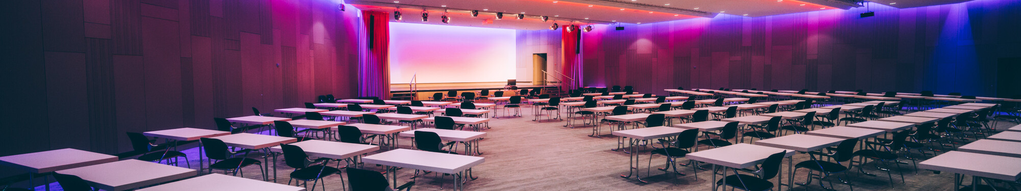 Stühle und Tische in einem lila beleuchteten Veranstaltungsraum im CCD Congress Center Düsseldorf