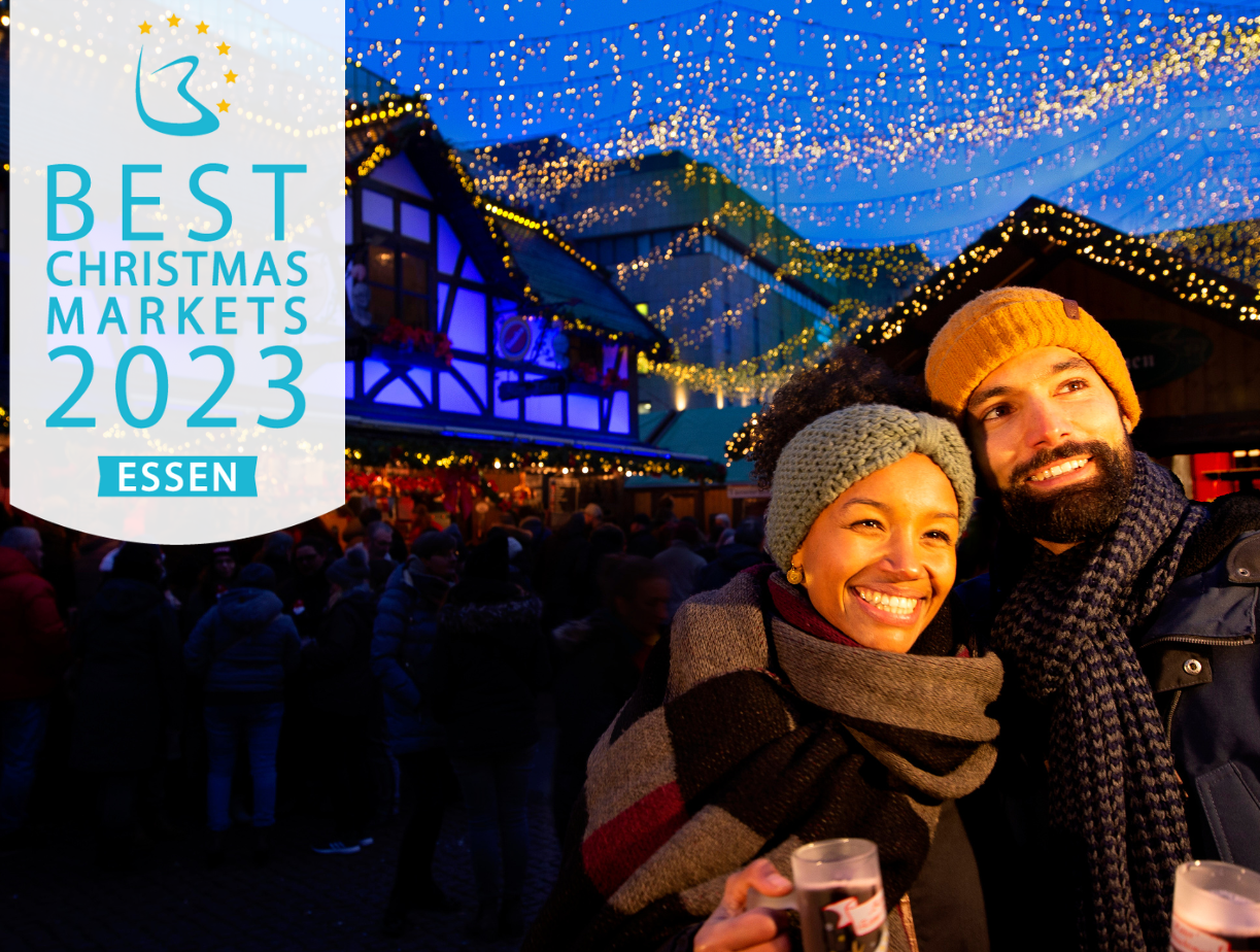 Ein Mann und eine Frau stehen auf dem Essener Weihnachtsmarkt. Auf dem Bild steht: Best Christmas Markets 2023 - Essen.