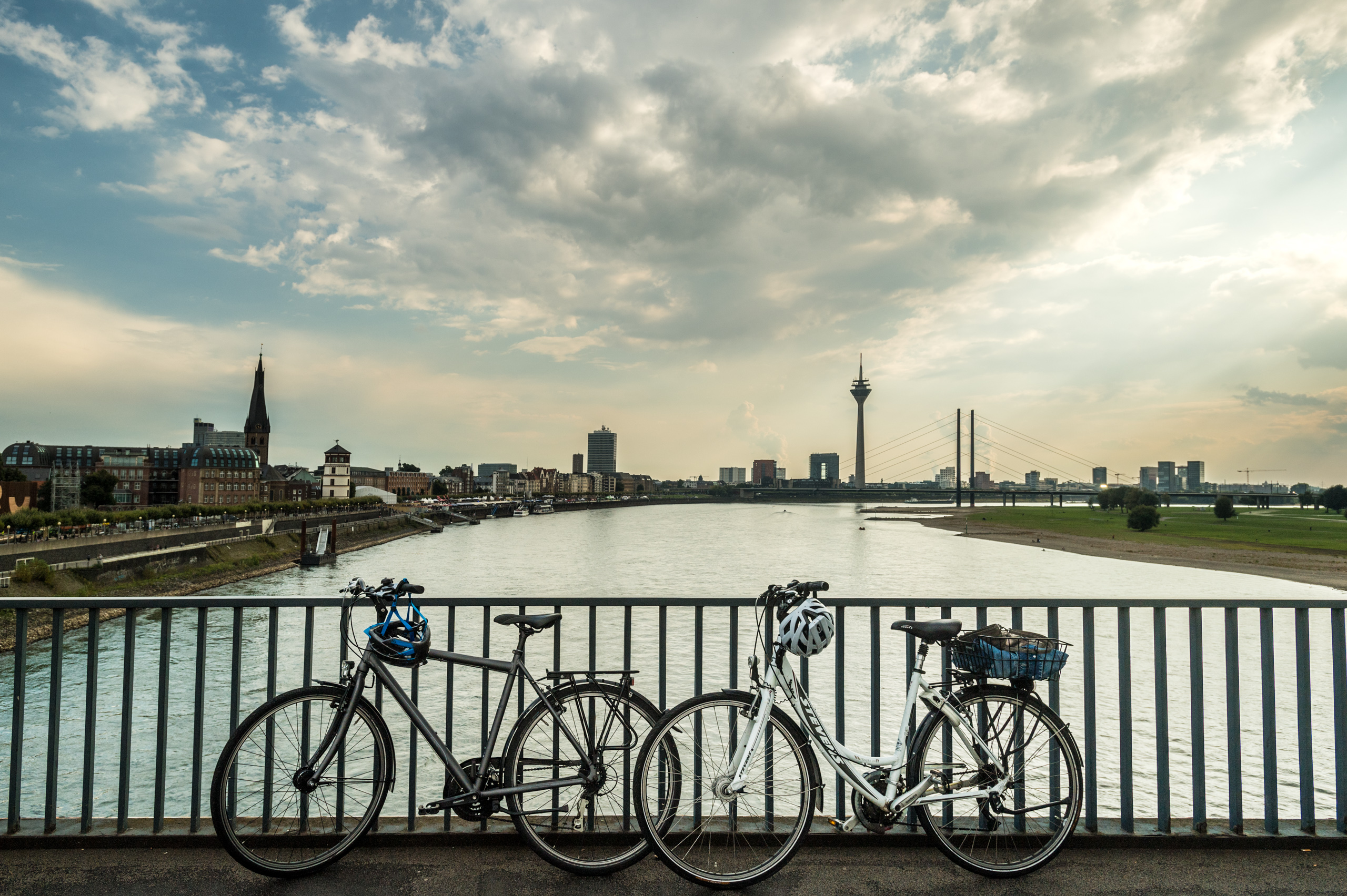 Blick auf die Skyline von Düsseldorf mit Rheinturm. Im Vordergrund stehen zwei Fahrräder auf einer Brücke über den Rhein. 