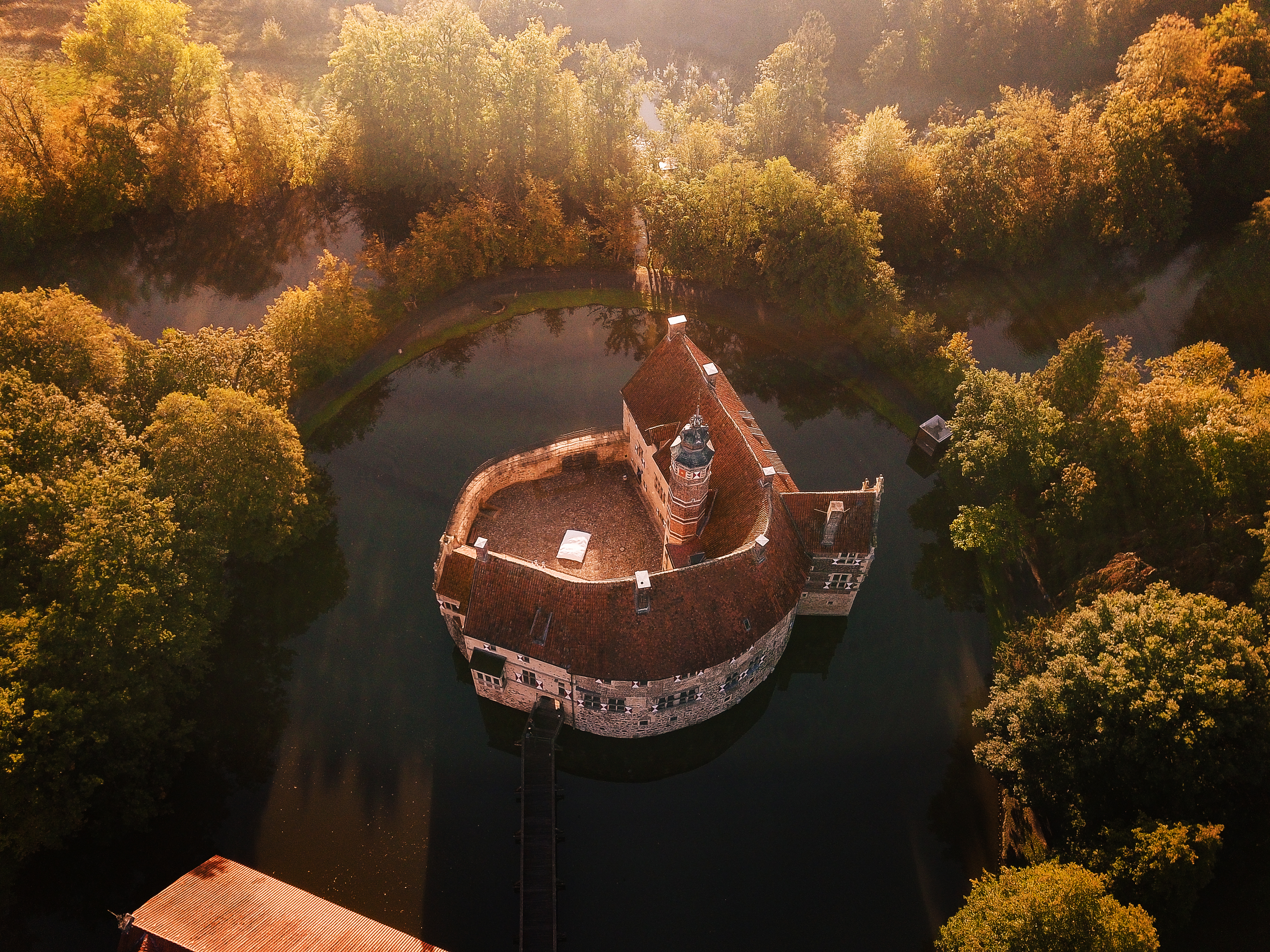 Blick von oben auf Burg Vischering in Lüdinghausen im Münsterland, umgeben von einem Wassergraben und Bäumen.  