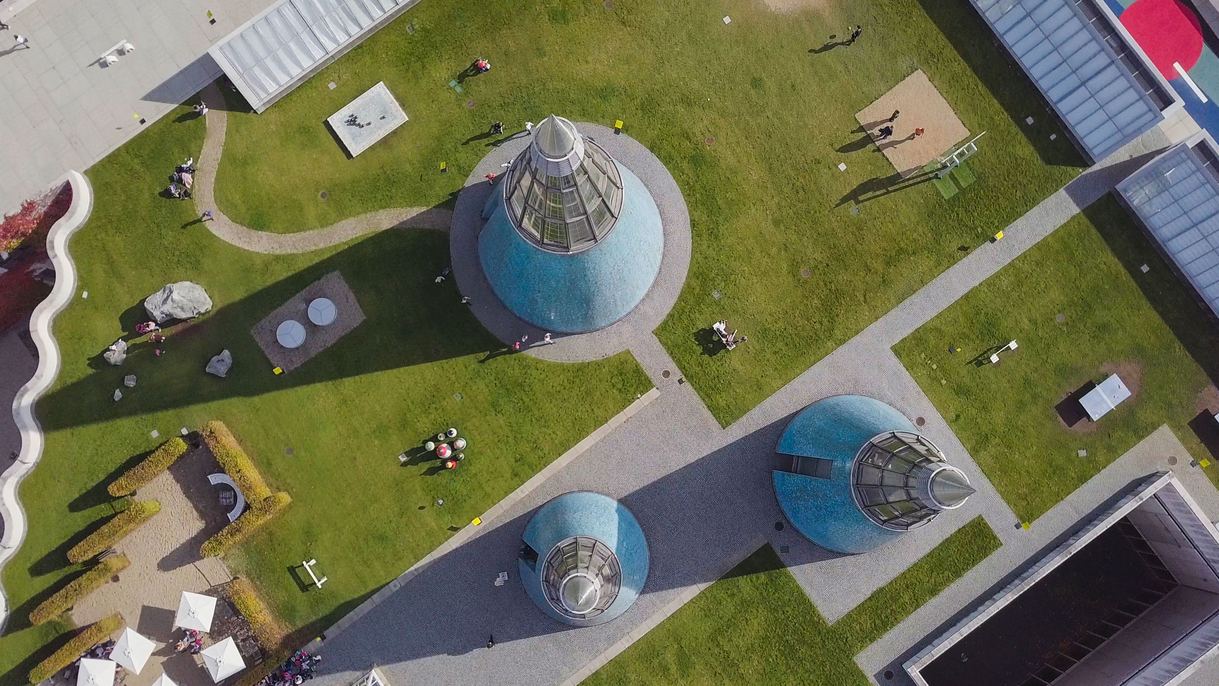 Blick von oben das begrünte und begehbare Dach der Bundeskunsthalle in Bonn mit drei bläulichen, zugespitzten Lichtkegeln. 