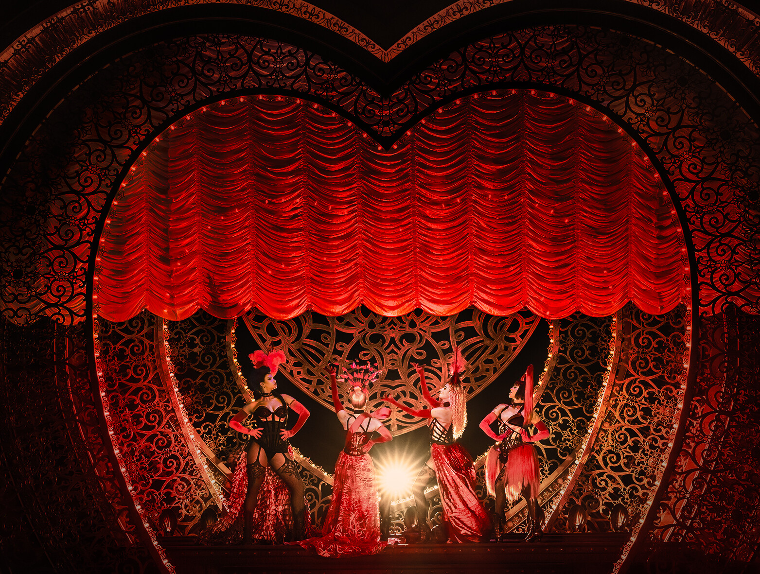 Szene aus dem Musical Moulin Rouge in Köln: Vier aufreizend angezogene Frauen stehen vor einem roten herzförmigen Vorhang.