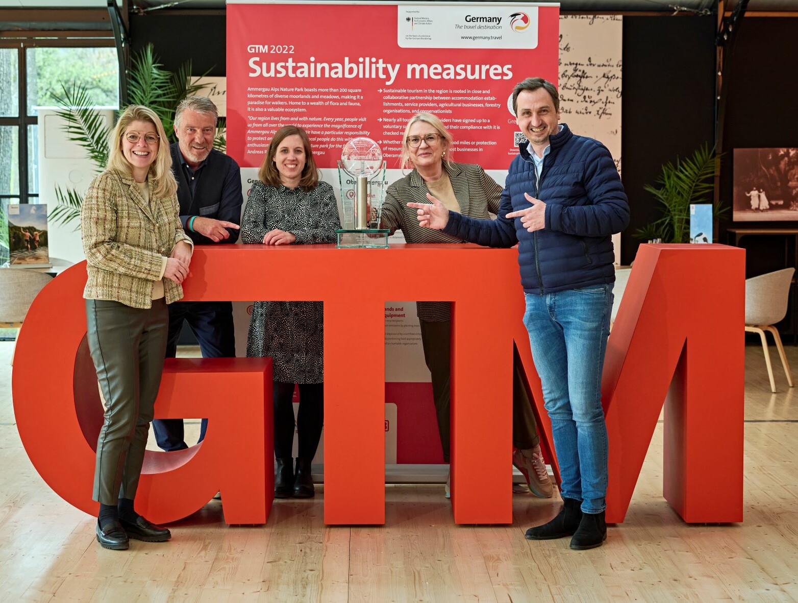 Pokalübergabe an den nächsten Ausrichter des GTM, Essen Marketing. v.l.: Julia Grundmann (DZT), Andreas Wietheger (Ruhr Tourismus), Julia Bauer (Tourismus NRW), Petra Hedorfer (DZT) und Richard Röhrhoff (Essen Marketing) © DZT/Jens Wegener Auf dem roten Schriftzug "GTM" steht der Pokal für den nächsten Ausrichter des GTM. Um den Schriftzug stehen Julia Grundmann (DZT), Andreas Wietheger (Ruhr Tourismus), Julia Bauer (Tourismus NRW), Petra Hedorfer (DZT) und Richard Röhrhoff (Essen Marketing).