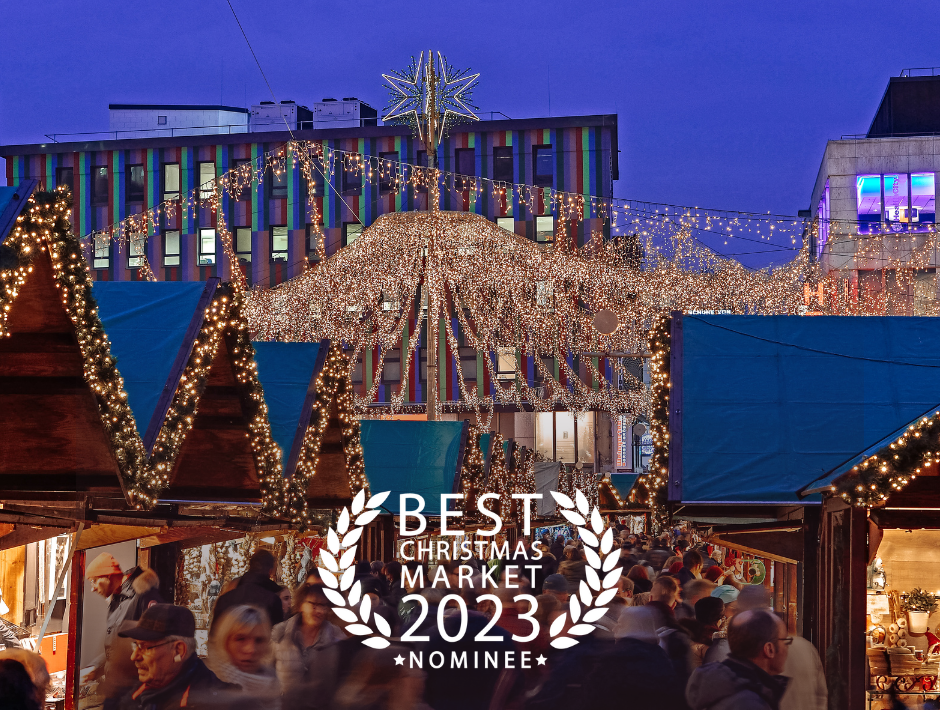 Beleuchtete Buden und viele Menschen auf dem Weihnachtsmarkt in Essen. Auf dem Bild steht: Best Christmas Market 2023 Nominee.