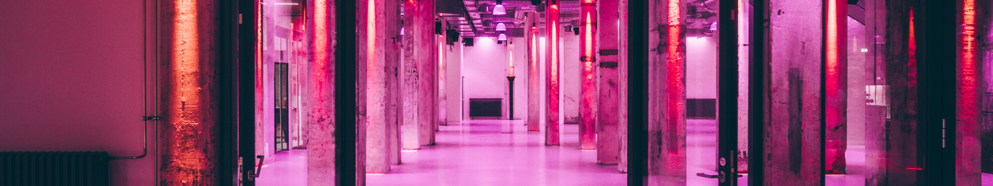 Die Stützpfeiler im Foyer der Grand Hall Zollverein in Essen sind mit rotem und violettem Neonlicht beleuchtet.  
