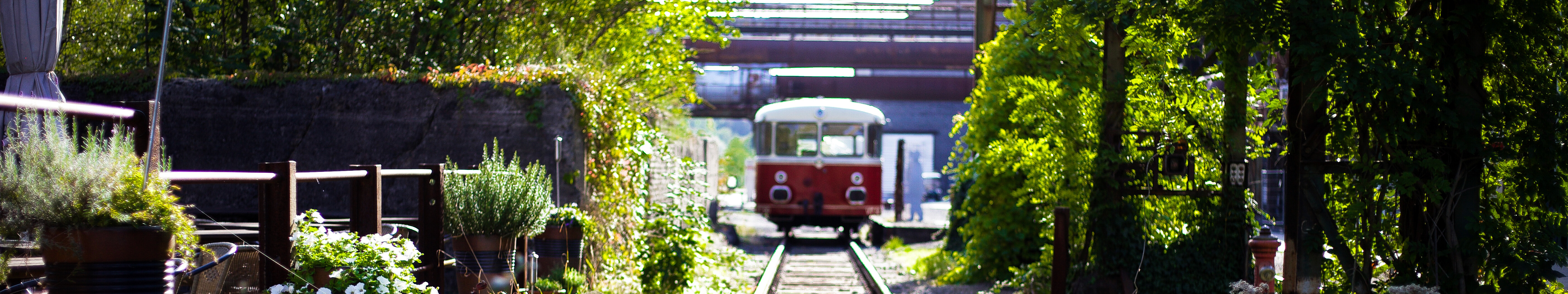 Ein alter Eisenbahnwaggon fährt auf den Gleisen durch die begrünte Außenanlage des LWL-Industriemuseums Henrichshütte in Hattingen. 