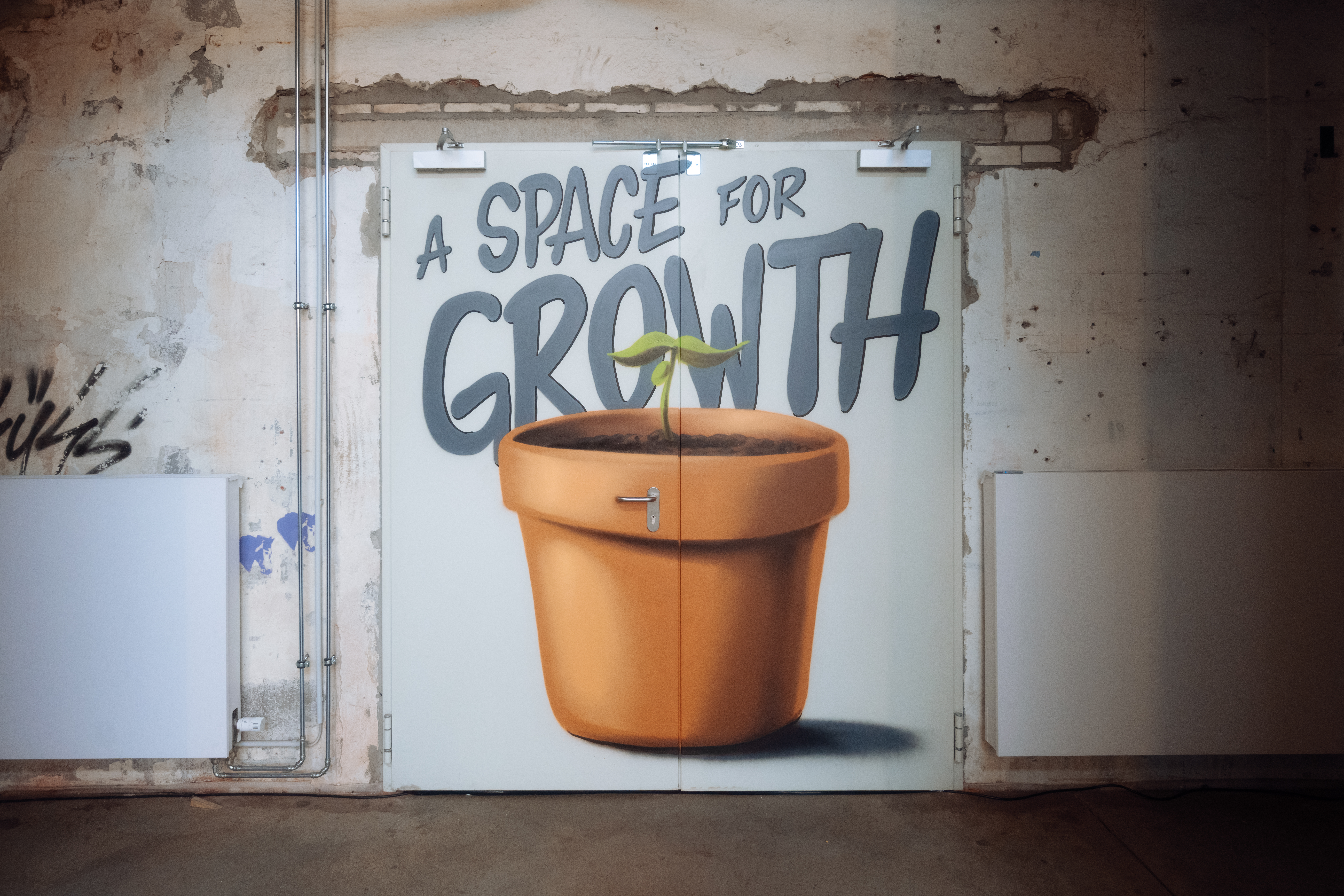 Blick in den Co-Working-Space "Codeks" in Wuppertal. Auf eine Tür ist ein Topf mit einer Pflanze gemalt, über dem steht "A Space for Growth". 