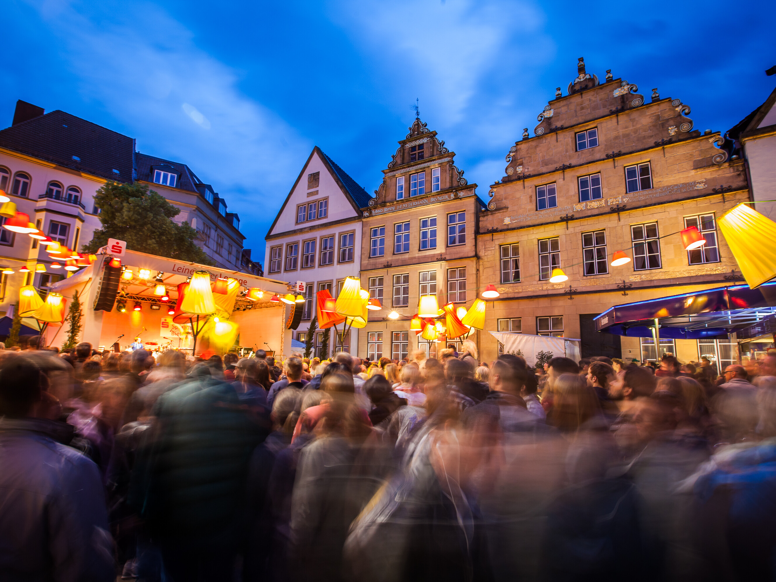 Menschen feiern vor den historischen Fassaden der Bielefelder Innenstadt in der Abenddämmerung. Der Leineweber-Markt lockt alljährlich Tausende in die Innenstadt. 