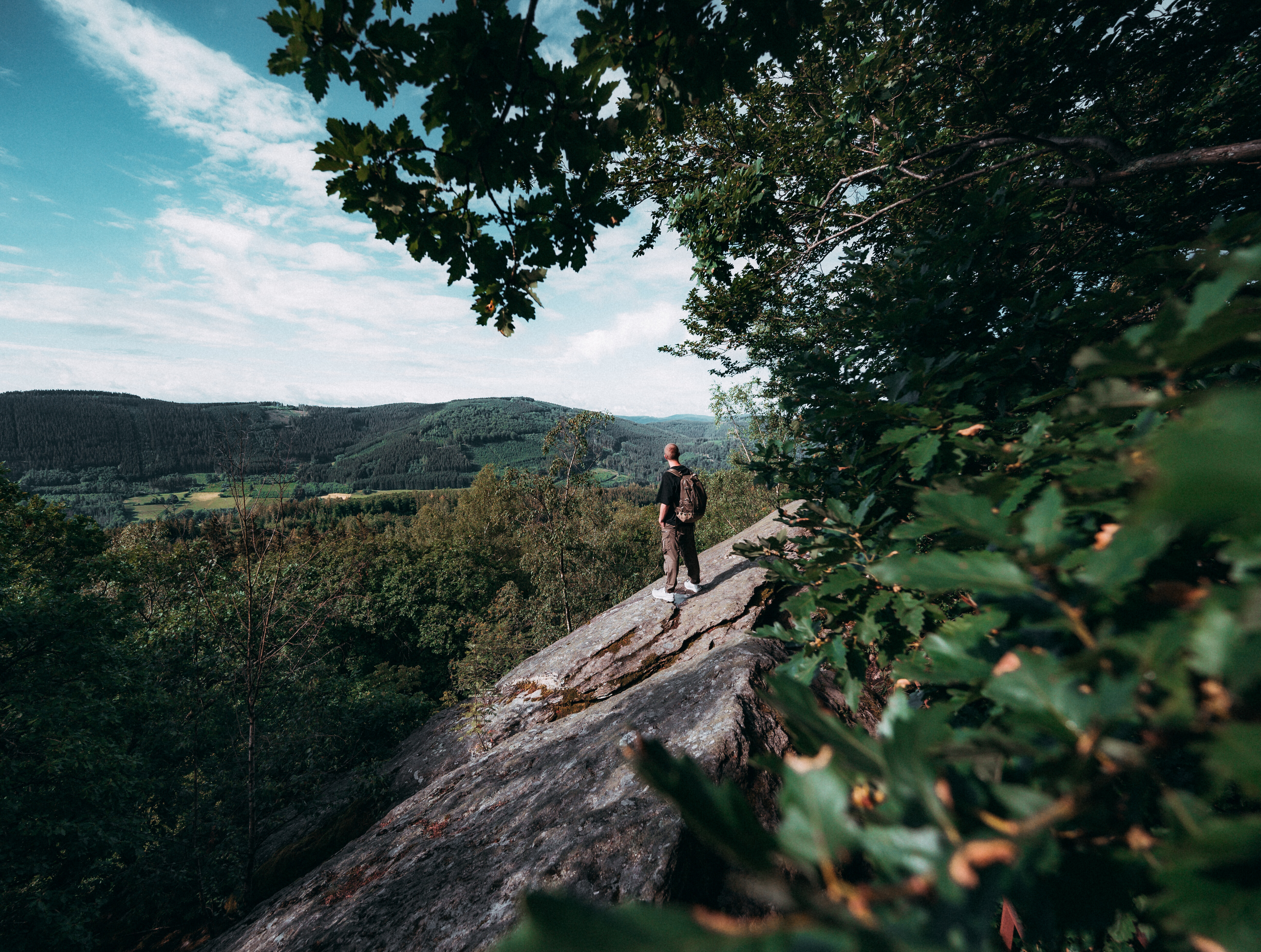 Ein Wanderer steht auf einem Felsvorsprung am Walderlebnispfad Saalhausen im Sauerland und blickt über die bewaldeten Hügel. 
