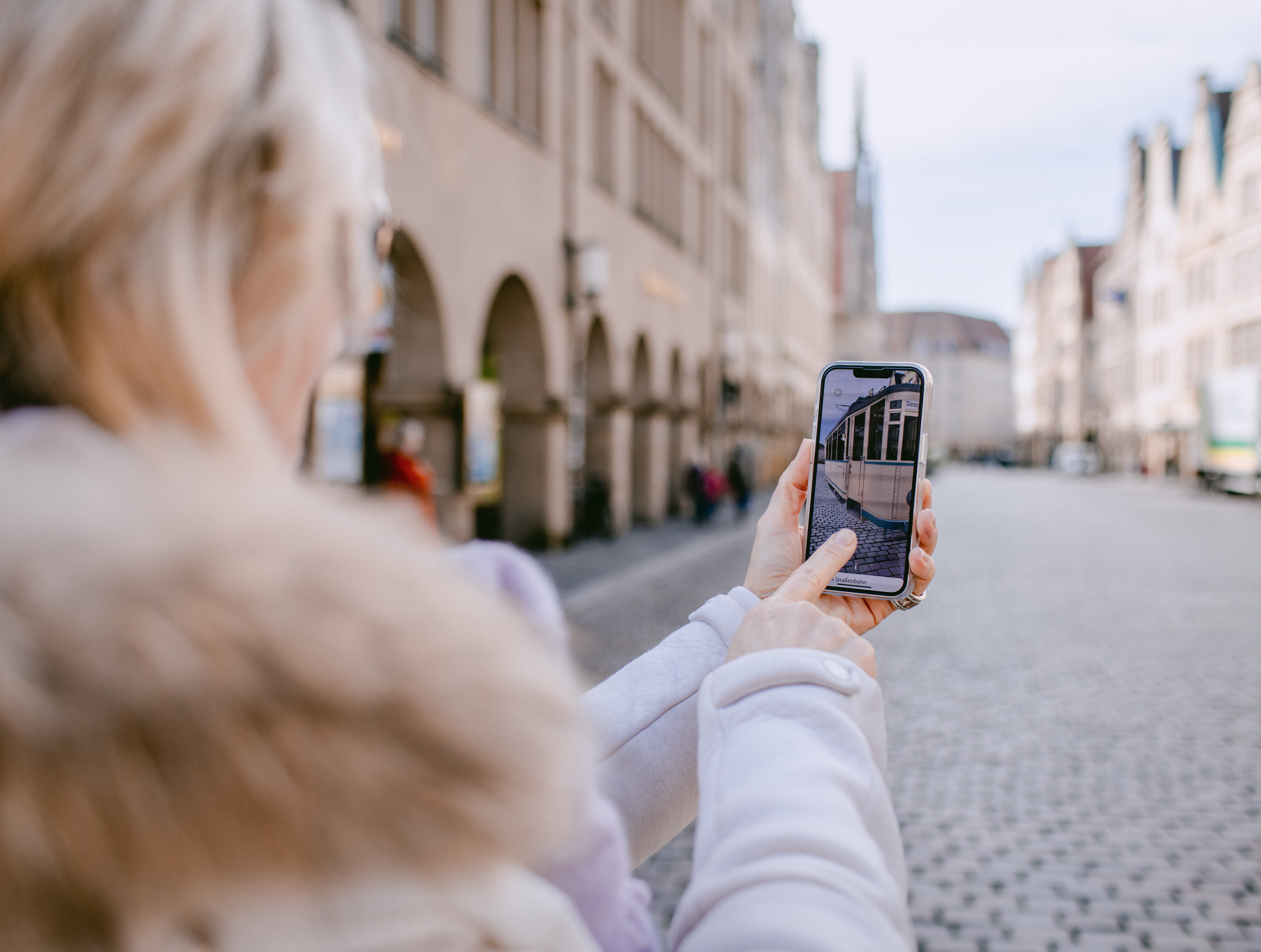 Eine Frau schaut auf ihr Handy, auf der die neue Stadtführungs-App aus Münster eine historische Straßenbahn wiederaufleben lässt. © Stadt Münster/Kuiter