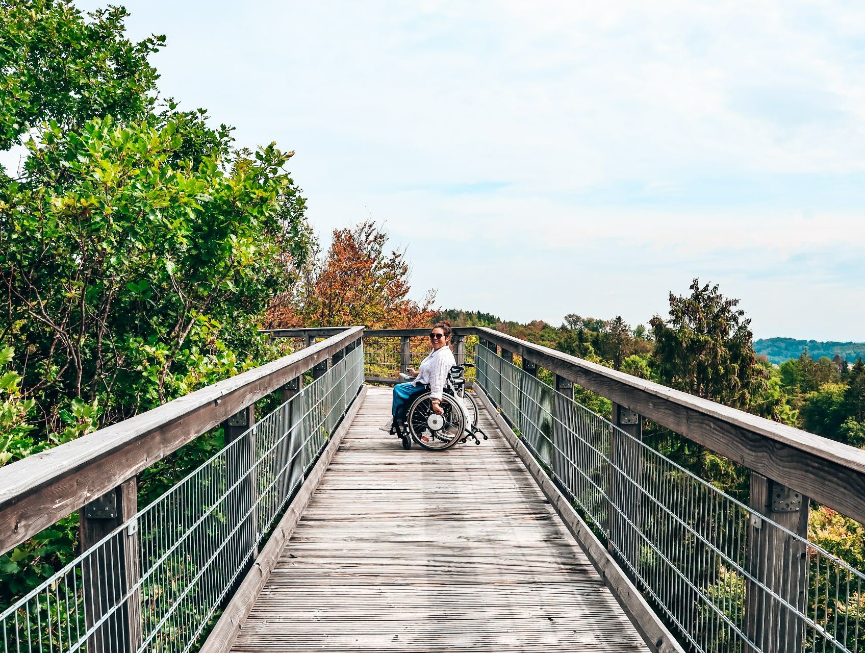 Eine Rollstuhlfahrerein auf dem hölzernen Steg des Baumwipfelpfads Panabora.  © wheeliewanderlust