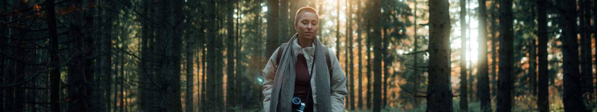 Eine Frau läuft durch einen Fichtenwald im Rothaargebirge. Durch die Bäume scheint die Sonne. 
