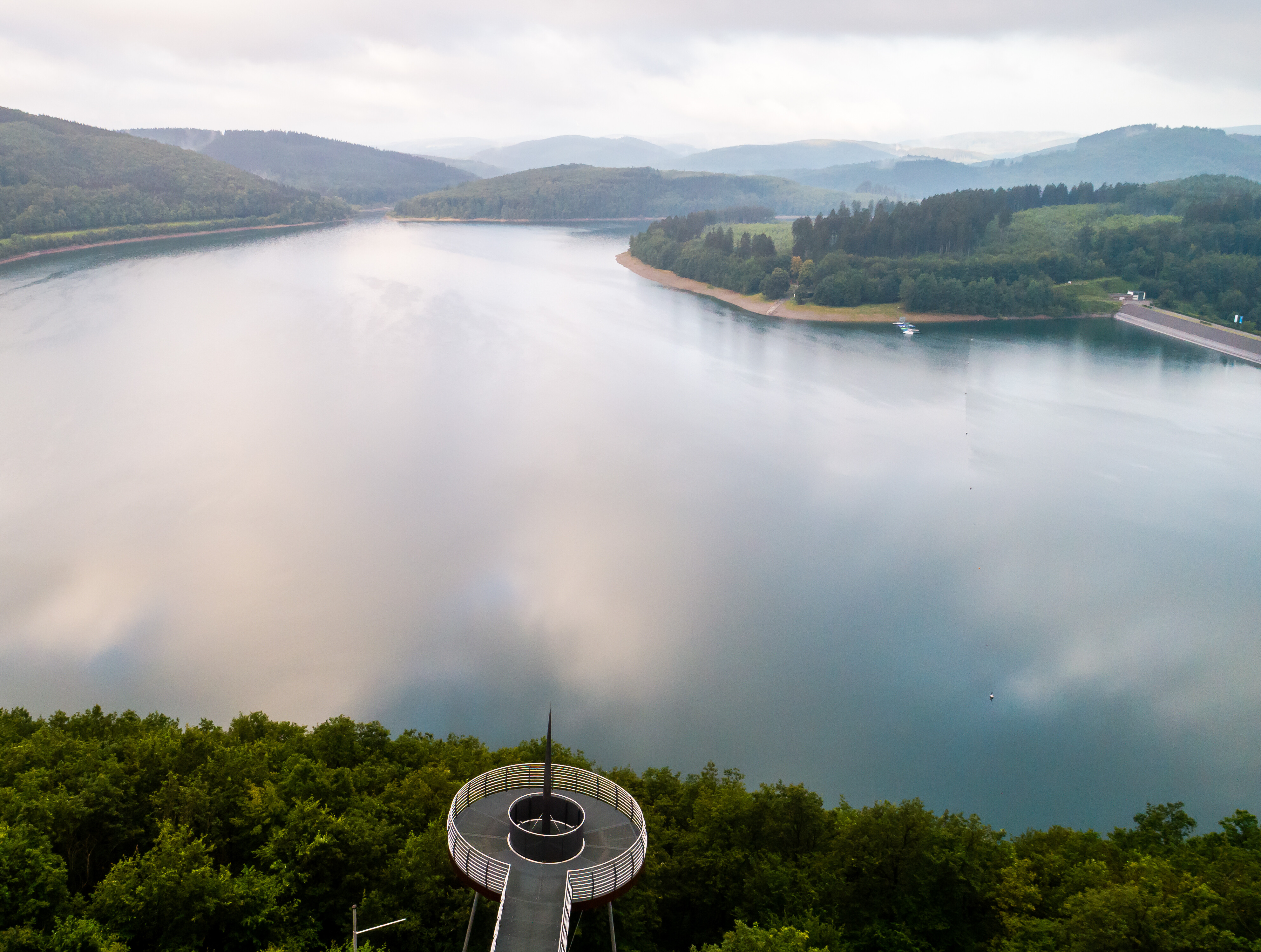 Luftaufnahme des Biggesees, der von Wäldern eingerahmt wird. Im Vordergrund ist eine Aussichtsplattform zu sehen.