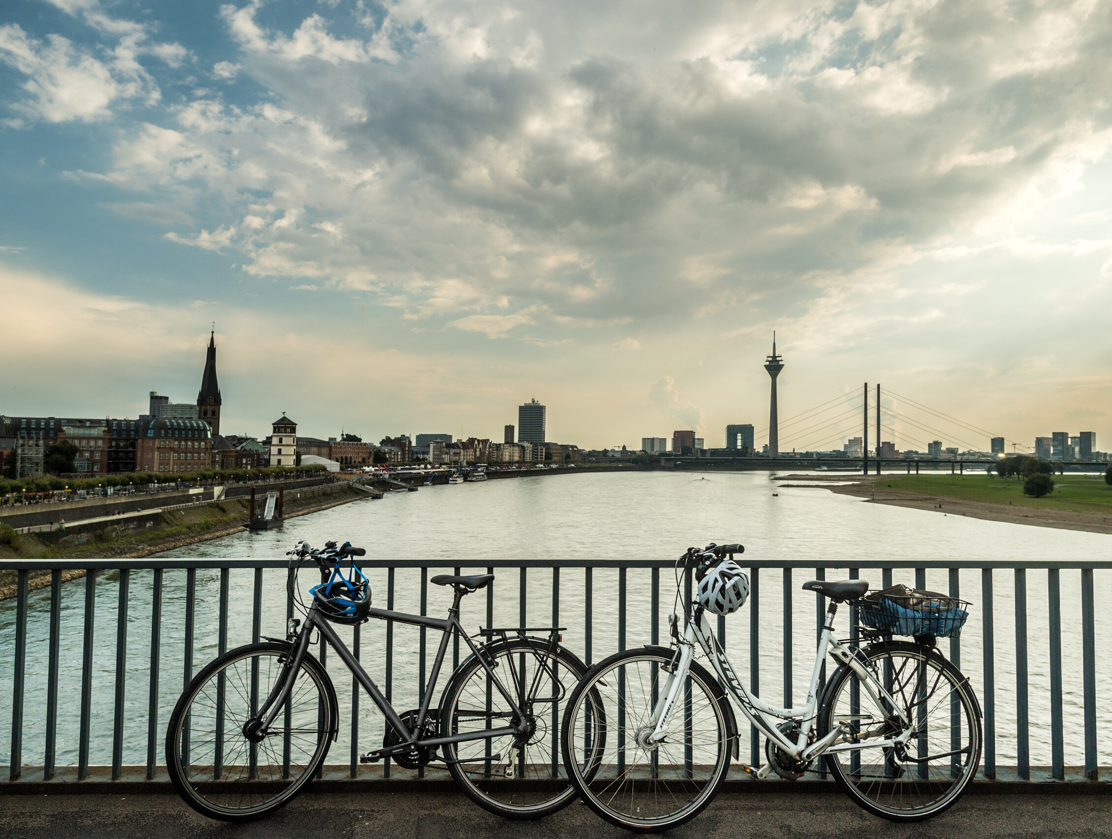Blick auf die Skyline von Düsseldorf mit Rheinturm. Im Vordergrund stehen zwei Fahrräder auf einer Brücke über den Rhein. 