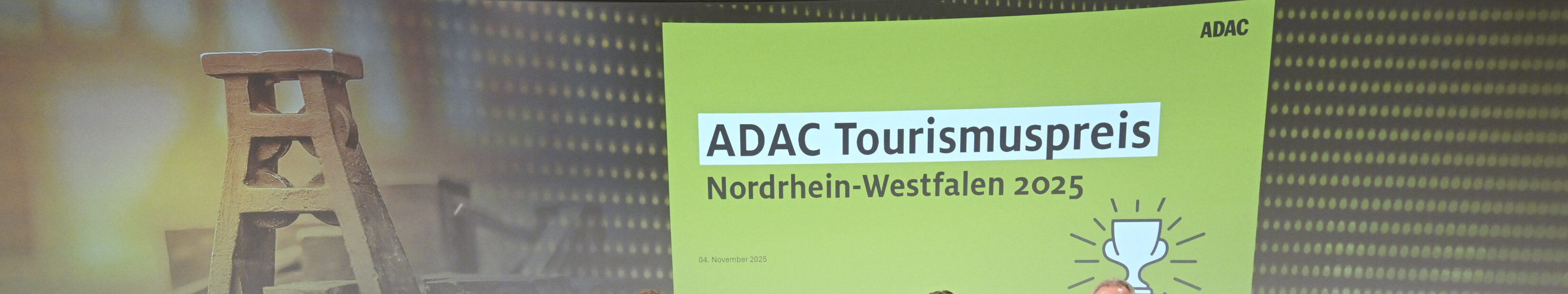 Gewinner des ADAC-Tourismuspreises NRW 2025 © Andreas Buck Die Gewinner des ADAC-Tourismuspreises NRW 2025 stehen im Halbkreis und halten ihre Urkunden in der Hand. Hinter sie sind Bilder von Zeche Zollverein und dem Logo des Tourismuspreises projiziert.