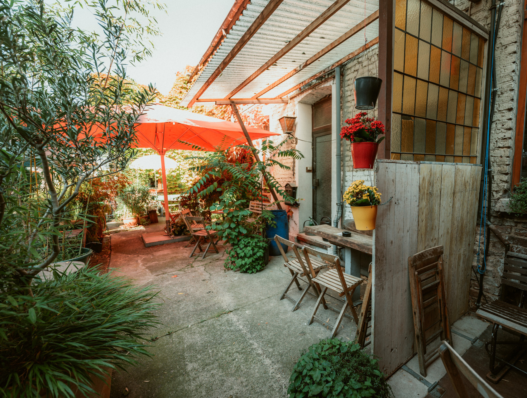 Café in Düsseldorf © Tourismus NRW e.V./Johannes Höhn Teilweise überdachte Terrasse mit Holzstühlen und -tischen, einem großen roten Sonnenschirm und vielen Grünpflanzen
